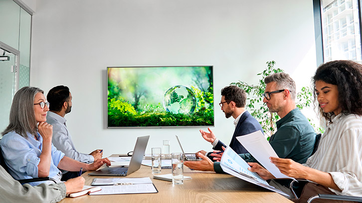Personen sitzen um einen Meetingtisch mit Bildschirm